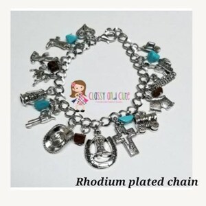 May include: A silver charm bracelet with a rhodium plated chain and various charms, including a horseshoe, a cross, a boot, a cowboy hat, and a train. The charms are accented with turquoise stones.