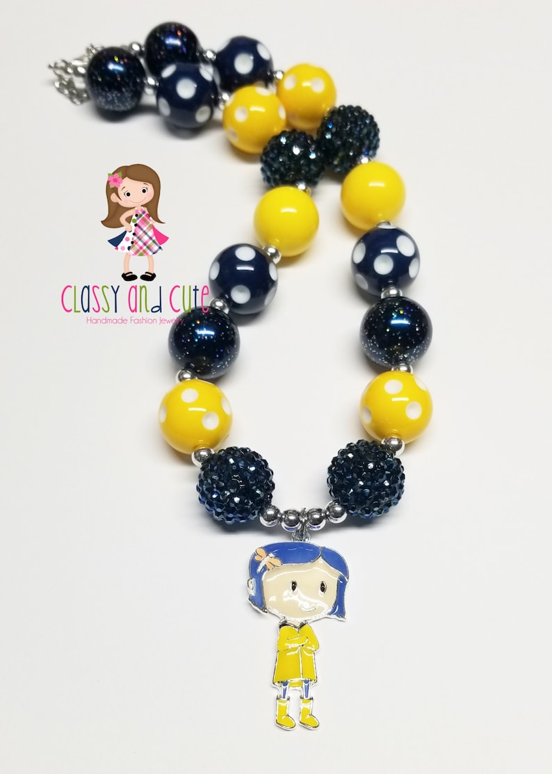 May include: A yellow and blue beaded necklace with a charm of a girl in a yellow raincoat. The necklace has white polka dots on the yellow beads and blue beads with glitter.
