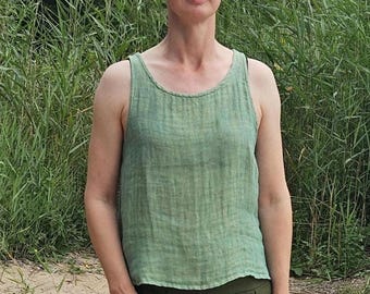 May include: A sleeveless sage green linen tank top with a round neckline and a textured, slightly sheer fabric finish. The garment features a relaxed fit with a straight hemline, showcasing a natural weave pattern throughout the light green material.