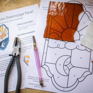 May include: A stained glass pattern for a sun and moon dreamscape panel. The pattern is printed on white paper with black lines and numbers. The pattern includes a sun, moon, and clouds. The difficulty level is listed as expert.