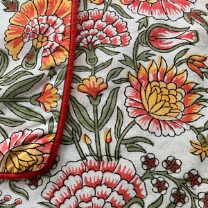 May include: White fabric with a red border and a floral pattern. The pattern features red, yellow, and green flowers with intricate details.