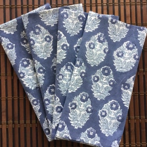 May include: Set of four blue cotton napkins with a white floral pattern. The napkins are folded and arranged on a bamboo surface.