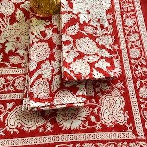 May include: Red and white cotton tablecloth with a floral pattern. The tablecloth has a white border with a repeating zig-zag design.