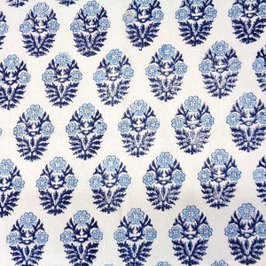May include: A white fabric featuring a repeating pattern of floral motifs. Each motif consists of a dark blue leafy base topped with light blue flowers, arranged in a structured grid across the surface of the textile material.