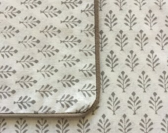 May include: A close-up of a white fabric with a repeating pattern of small gray stylized trees. The fabric has a brown border.