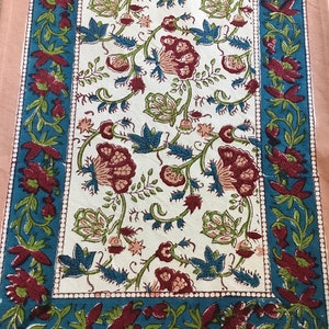 May include: A rectangular floral table runner with a cream-colored center and a teal border. The center features a repeating pattern of burgundy flowers and green leaves. The border is adorned with burgundy floral designs. The runner is approximately 60 inches long.