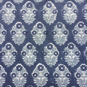 May include: A blue fabric with a white floral pattern. The pattern is a repeating design of stylized flowers with leaves.