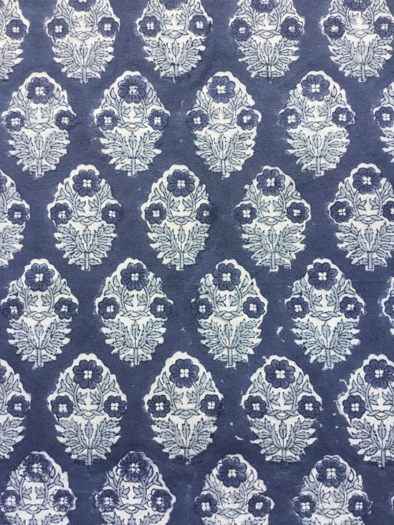 May include: A blue fabric with a white floral pattern. The pattern is a repeating design of stylized flowers with leaves.