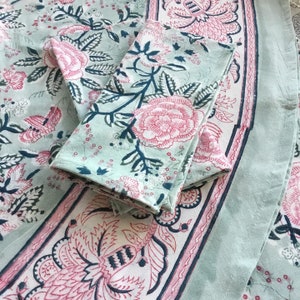 May include: A light blue floral tablecloth and matching napkins. The design features large pink roses, dark blue leaves, and a decorative border. The fabric is soft and appears to be cotton or linen, suitable for dining and home decor.