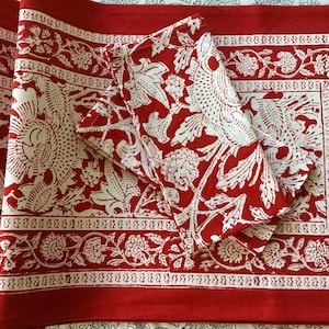 May include: Red and white floral patterned placemats and napkins. The placemats and napkins feature a repeating floral design with a border of smaller floral elements. The napkins are folded and stacked on top of the placemats.