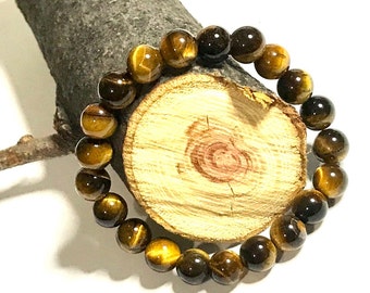 May include: A brown and gold tiger's eye gemstone bracelet with round beads. The bracelet is on a wooden surface.