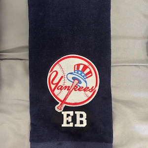 Könnte beinhalten: Marineblaues Handtuch mit dem Logo der New York Yankees, rot, weiß und blau gestickt. Das Logo ist ein Baseball mit dem Teamnamen. Die Initialen "EB" sind darunter gestickt. Das Handtuch hat eine Schlaufe zum Aufhängen.