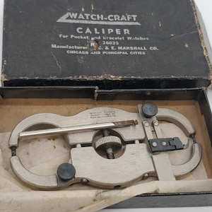 May include: A silver-toned metal Watch-Craft caliper for pocket and bracelet watches, featuring a central adjustment wheel and black knobs, housed in a black cardboard box with white text reading Watch-Craft Caliper and C. & E. Marshall Co.
