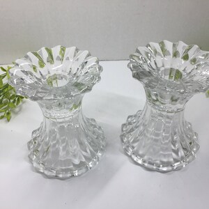 May include: Two clear glass candle holders with a fluted design. The holders are empty and have a round base.