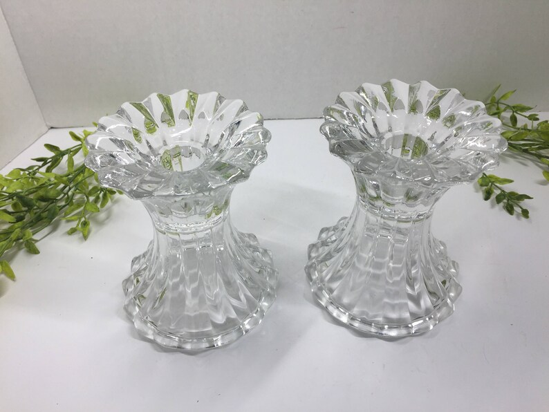 May include: Two clear glass candle holders with a fluted design. The holders are empty and have a round base.