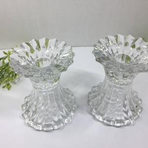 May include: Two clear glass candle holders with a fluted design. The holders have a wide, scalloped top and a round base.