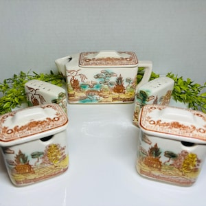 May include: A set of four vintage ceramic tea and sugar containers. The teapot is decorated with a brown and green floral pattern. The sugar containers are decorated with a similar pattern and have lids.