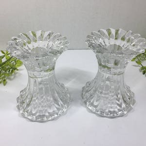 May include: Two clear glass candle holders with a fluted design. The holders have a wide, scalloped top and a flared base.