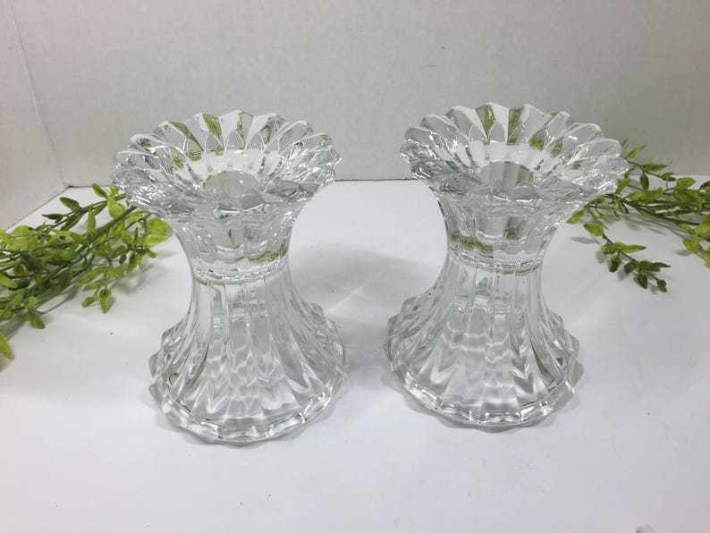 May include: Two clear glass candle holders with a fluted design. The holders have a wide, scalloped top and a flared base.
