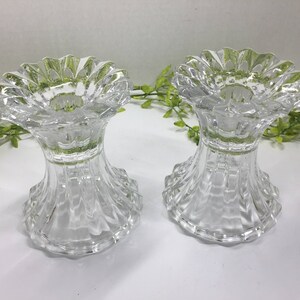 May include: Two clear glass candle holders with a fluted design. The holders have a scalloped top and a wide base.
