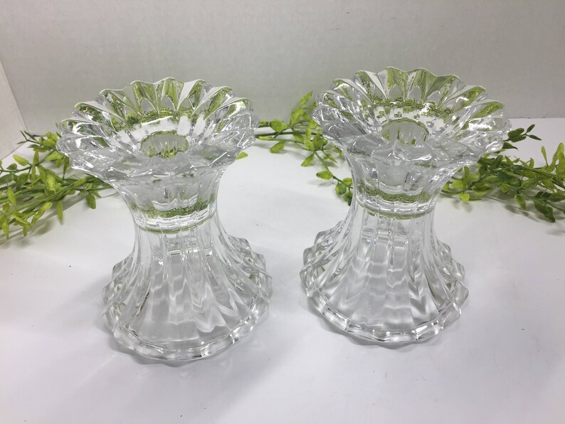 May include: Two clear glass candle holders with a fluted design. The holders have a scalloped top and a wide base.
