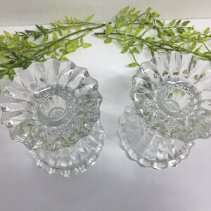 May include: Two clear glass candle holders with a fluted design. The holders are empty and ready to be used.