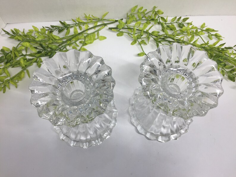 May include: Two clear glass candle holders with a fluted design. The holders are empty and ready to be used.