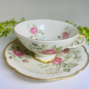 May include: A vintage teacup and saucer set with a delicate floral pattern featuring pink roses and green leaves. The set is made of white porcelain with a gold trim.