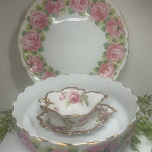 May include: A set of three white porcelain bowls with pink rose floral designs and gold trim. The bowls are nested inside each other, with the smallest bowl on top.