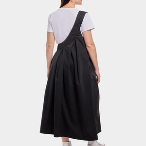 Puede incluir: Un vestido midi negro con una camiseta blanca debajo. El vestido tiene un dise&ntilde;o asim&eacute;trico &uacute;nico y una falda plisada.