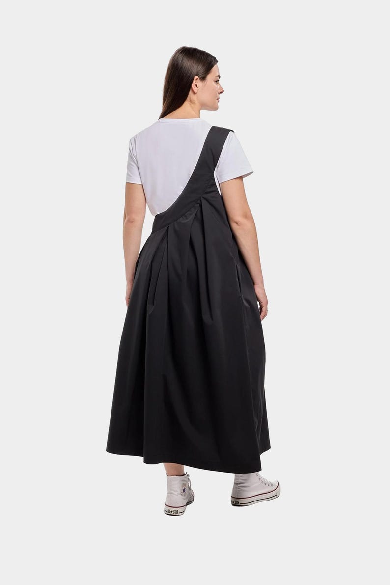 Puede incluir: Un vestido midi negro con una camiseta blanca debajo. El vestido tiene un dise&ntilde;o asim&eacute;trico &uacute;nico y una falda plisada.