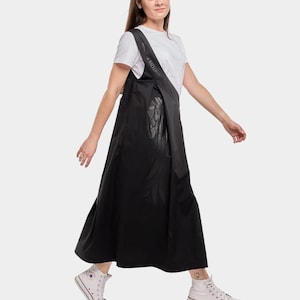 Puede incluir: Una mujer lleva un vestido maxi negro con una camiseta blanca debajo. El vestido tiene un dise&ntilde;o &uacute;nico con un panel de cuero negro en la parte delantera. Lleva zapatillas blancas.