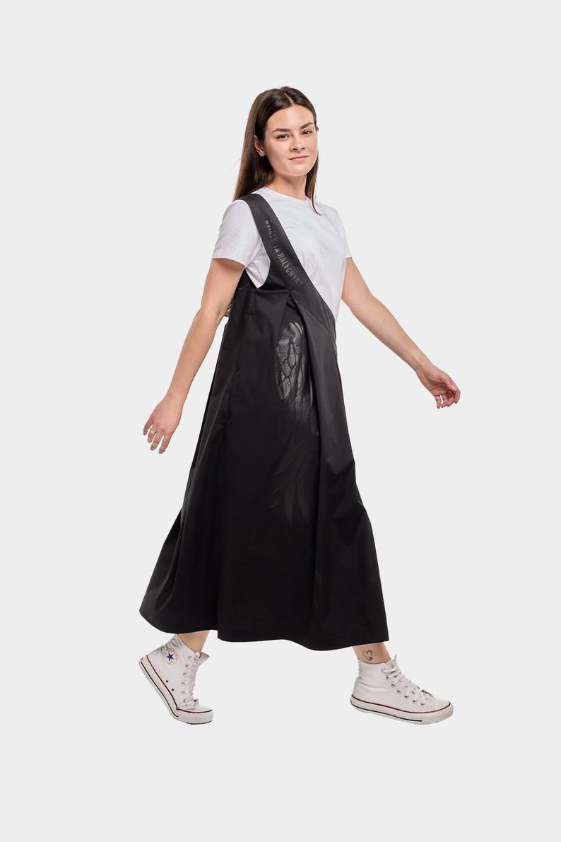 Puede incluir: Una mujer lleva un vestido maxi negro con una camiseta blanca debajo. El vestido tiene un dise&ntilde;o &uacute;nico con un panel de cuero negro en la parte delantera. Lleva zapatillas blancas.