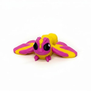 May include: A 3D-printed insect figurine in bright colors. The body is yellow, with a pink head and wings. The wings have yellow stripes. The insect has large, black eyes and small pink legs. The figurine is on a white background.