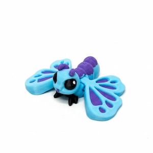 May include: A 3D-printed, stylized insect figurine. The body is light blue with purple segments and antennae. The wings are light blue with purple accents. The insect has black eyes and legs. The figurine is on a white background.