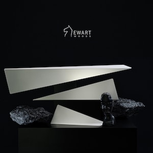 May include: A modern art display featuring geometric white shapes, black rocks, and a black bust against a black background. The logo "Ewart Woods" is visible in the upper left corner.