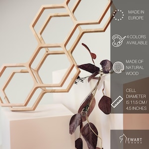 May include: A light-colored wooden honeycomb wall shelf with three hexagonal cells. Text on the right indicates it is made in Europe, available in 4 colors, made of natural wood, and has a cell diameter of 4.5 inches. The brand is Ewart Woods.