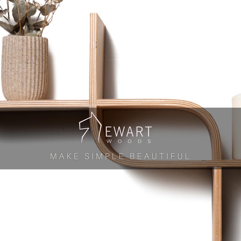 May include: A modern, light-colored wooden wall shelf with a unique, geometric design. The shelf features curved and straight lines, creating an open, airy aesthetic. A beige textured vase with dried plants sits on the shelf. The text "EWART WOODS MAKE SIMPLE BEAUTIFUL" is visible.