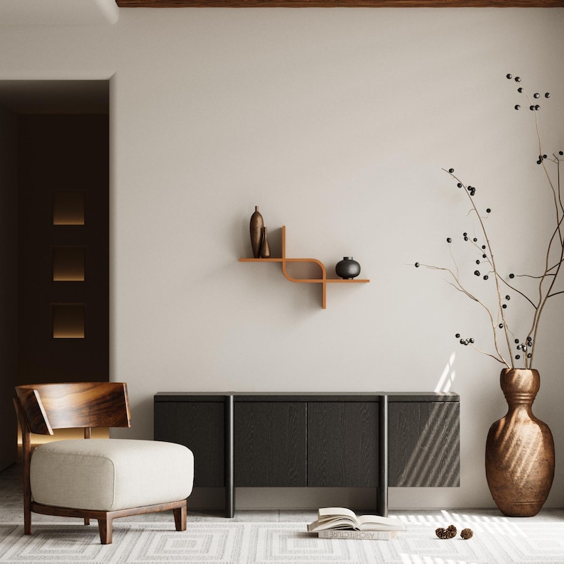 May include: A modern living room scene featuring a dark gray cabinet, a wooden chair with a cream-colored cushion, and a decorative wooden shelf with vases. A large bronze vase holds branches with berries. The room has a neutral color palette.