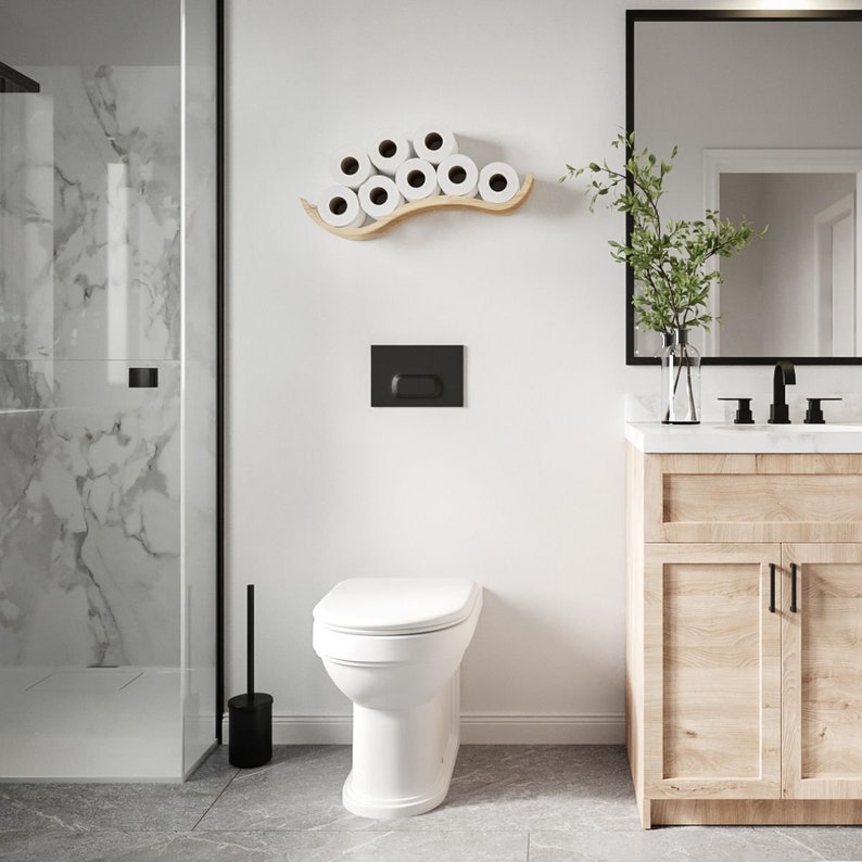 A modern bathroom featuring a wooden wall-mounted toilet paper holder with a wave design, displaying several rolls of toilet paper. The bathroom includes a walk-in shower, a wooden vanity, and a sleek mirror,