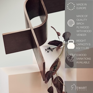 May include: A modern, dark brown wooden sculpture with a unique, intersecting design. The sculpture is made of birch plywood with wood veneer and has a weight capacity of 11 lbs. The image also includes text that says "Made in Europe."