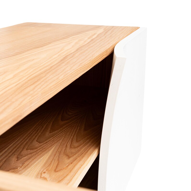 K&ouml;nnte beinhalten: Ein wei&szlig;er und naturfarbener Schrank mit einer gebogenen Front und offenen Regalen. Der Schrank ist aus massivem Holz gefertigt und hat ein modernes Design.