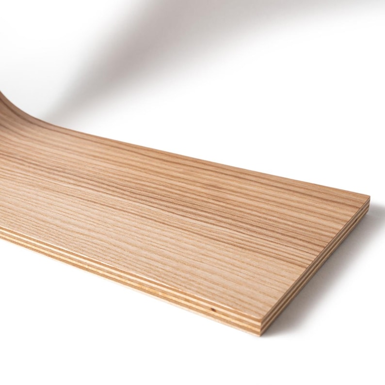 May include: A curved, light-colored wooden board with visible grain. The board has a rectangular shape and appears to be made of layered wood. The wood has a natural, light brown color and a smooth finish. The board is set against a white background.