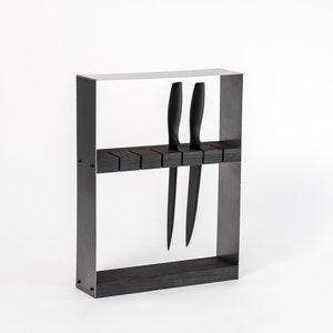 A sleek, modern knife block featuring a black metal frame and dark wooden insert, holding black-handled knives in evenly spaced horizontal slots.