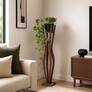Walnut tall indoor plant stand styled between a cream sofa and wooden TV unit in a warm-toned living room. Pot with trailing plant sits at eye level on the stand. Shows how the 118cm pillar stand fits naturally in a Scandinavian lounge.