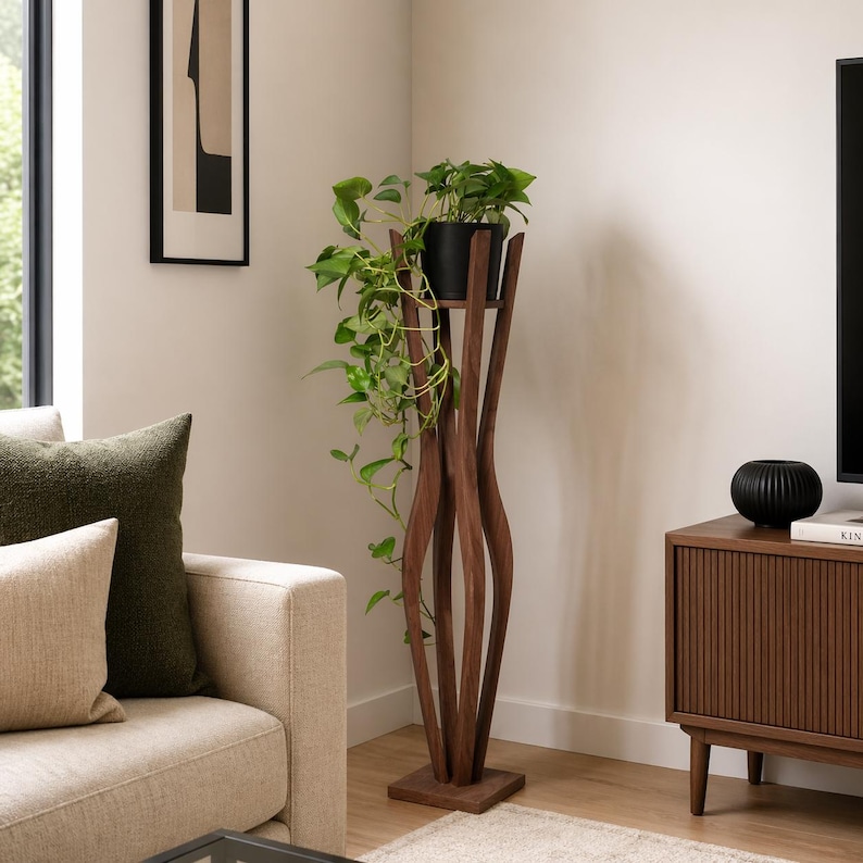 Walnut tall indoor plant stand styled between a cream sofa and wooden TV unit in a warm-toned living room. Pot with trailing plant sits at eye level on the stand. Shows how the 118cm pillar stand fits naturally in a Scandinavian lounge.