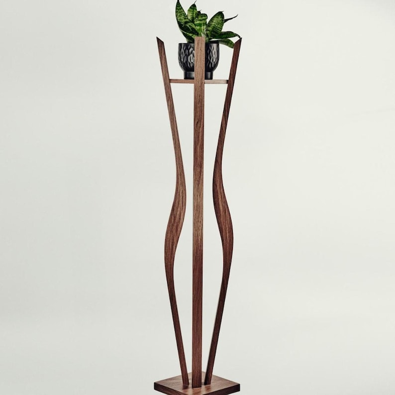 May include: A tall, dark brown wooden plant stand featuring three curved, vertical supports that rise from a square base to hold a small, circular platform. A black, textured ceramic pot containing a green snake plant sits on top.