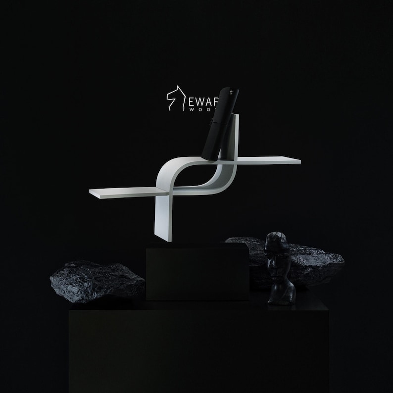May include: A white, modern, curved wooden shelf with a black phone. The shelf has a unique design with a horizontal surface and a vertical section to hold the phone. The background is black, with a black box and rocks.