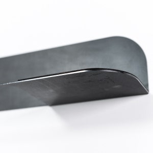 May include: A black metal shelf with a curved edge. The shelf is designed to be mounted on a wall.