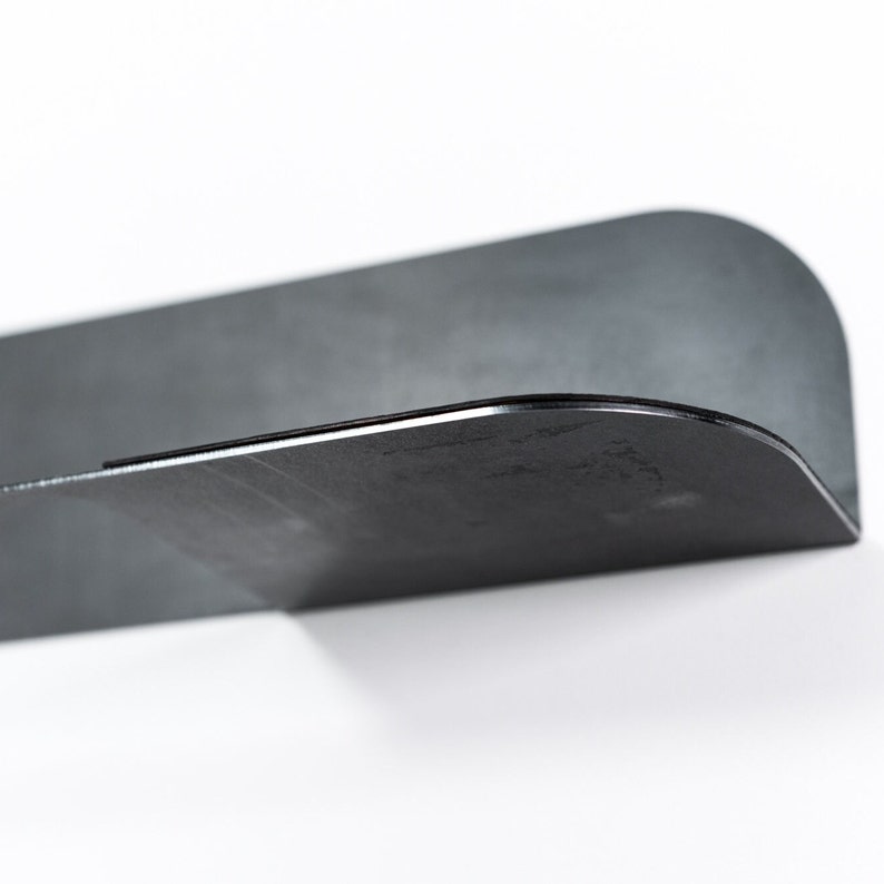 May include: A black metal shelf with a curved edge. The shelf is designed to be mounted on a wall.